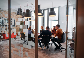 Fototapeta premium In a sleek glass office space, a team of business professionals engage in lively discussions and exchange strategic ideas, showcasing collaboration and innovation at the heart of modern corporate