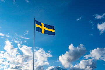 Swedish flag on blue sky with white clouds. 6 June. Flag of Sweden  in sunny rays high on the flagpole. Celebration Holiday National Day Festive. Event. 