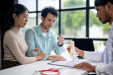 A doctor is showing a patient a model of a spine