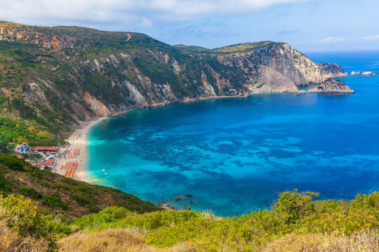 Petani Beach, Lixouri in Summer, on the Ionian island of Kefalonia, Greece, with orange umbrellas, sunbeds and clear blue sky and high mountains.  Space for copy, Horizontal.