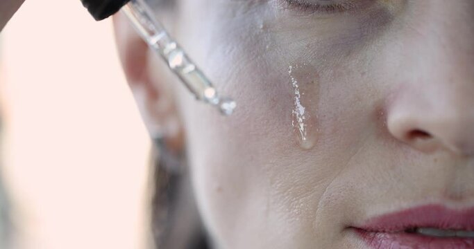 Woman applying essential oil dropper to face. Rejuvenation facial skin care concept