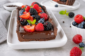 Delicious chocolate cream tart with fresh berry and mint on top on the plate on a gray background....