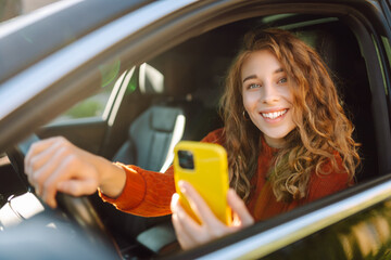 Young woman in a car using mobile phone. Leisure, travel, technology. Carsharing.