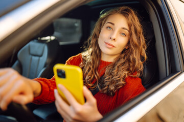 Young woman in a car using mobile phone. Leisure, travel, technology. Carsharing.