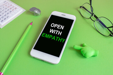 Open with empathy message written on the mobile phone screen. Beautiful green background. Glasses,...