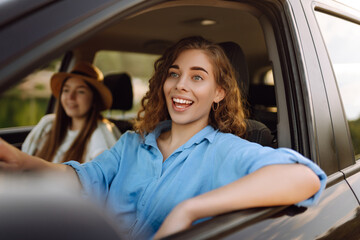 Two fun young women driving in a car in town laughing and smiling as they socialise together. Travel, tourism.