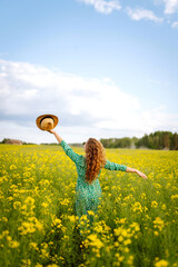 Beautiful woman in bright dress walking through flowering field, touching yellow flowers. Fashion,...