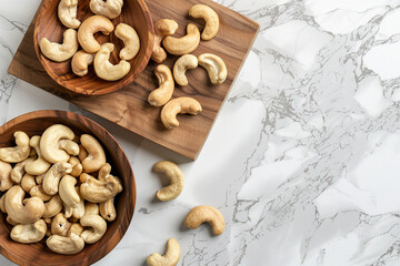 Fototapeta premium Top view of cashew nuts in wooden bowls on a kitchen board over a white marble background