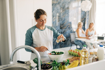 A woman prepares a salad for lunch with friends at home.