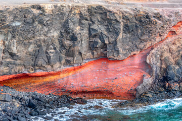 Cliff with a red flow of water running down it. Majestic rock formation overlooking the ocean