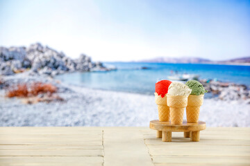 Ice cream in waffle cones on a wooden table. Blurry rocky and pebble beach background. Relaxing on the beach on a hot summer day.
