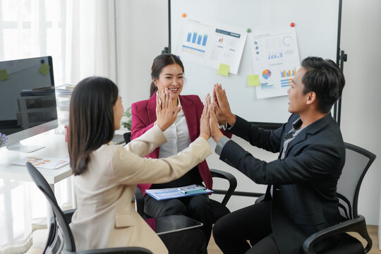 Three business professionals celebrating a successful meeting with a group high-five in a modern office setting.