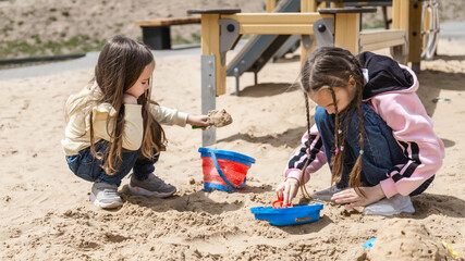 Pretty baby having fun on sunny warm summer day - Cute toddler girl playing in sand on outdoor playground with her sister
