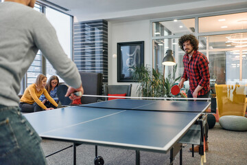  Business colleagues take a break from work to enjoy a game of table tennis, fostering teamwork and...