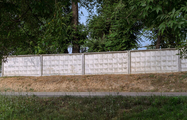 a white concrete fence, green trees and dry grass near the road