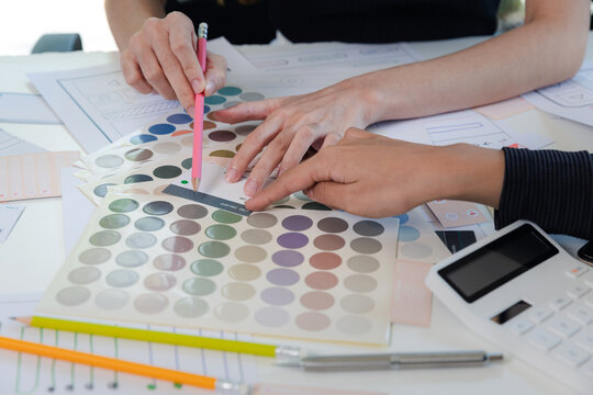 Women point to a color chart for home design. Graphic designers working on color chart at modern office.