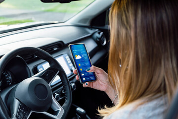 Woman in her car checking the weather forecast on an app on her mobile phone.