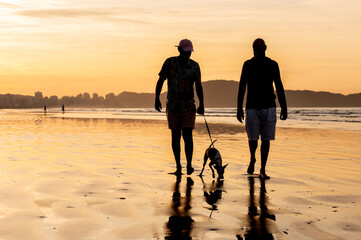 silhouette of a couple of homosexual men walking their dog on the beach at sunrise