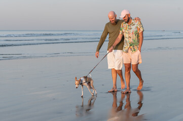 gay couple walking their dog on the beach at sunrise