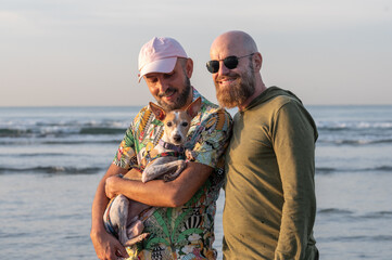 portrait of a gay couple with their dog on their lap on the beach at sunset