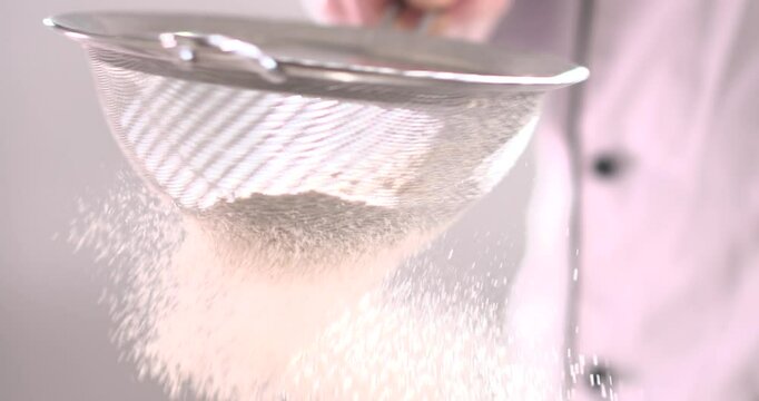The baker hits a sieve with his hand to sift the flour for the dough.
