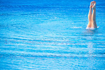 Female swimmer legs point up out of the water in swimming pool. Summer leisure, recreation, holiday, vacation, lifestyle or relax concept with copy space.