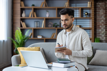 Learning online. Indian young male student sits at home on the sofa in front of a laptop with a...