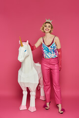 Woman in pink sparkly outfit poses with white unicorn on pink background.