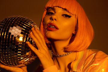 A woman with pink hair holds a disco ball in a dimly lit room.