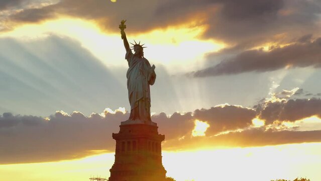 Sunset view of the Statue of Liberty with dramatic light rays shining through as the sun sets behind the Statue.