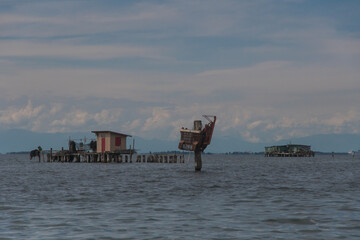 Panorama della laguna di Venezia con due case da pesca e un palo a cui sono legati dei vecchi macchinari da peschereccio per la raccolta delle cozze © Andrea Vismara