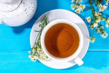 Herbal organic daisy camomile tea with fresh wild summer daisy chamomile flowers, in white cup, with teapot copy space