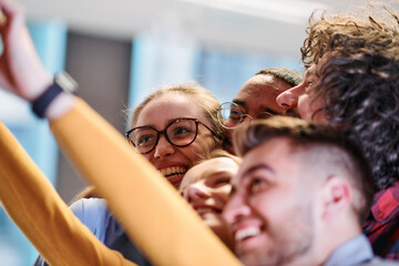 A diverse group of business professionals take a break from their tasks in a modern startup office to capture a creative selfie, showcasing teamwork and a vibrant workplace culture