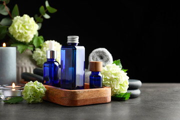 Spa composition. Cosmetic products, burning candles and hydrangea flowers on gray table against black background, space for text