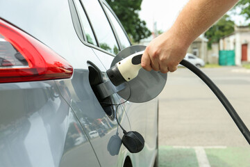 Man inserting plug into electric car socket at charging station outdoors, closeup