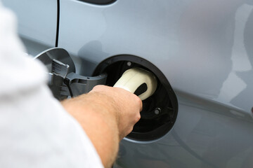 Man inserting plug into electric car socket at charging station outdoors, closeup