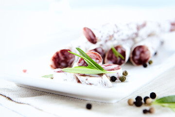 Sliced french salami with fresh rosemary on white background. Copy space.
