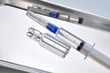 Syringes with needles and an ampoule in a stainless steel medical tray.