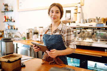 Young woman owner with tablet stands behind the counter of a coffee shop. Business concept....