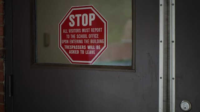 Extreme closeup of STOP sign on front door of public school telling visitors to report to office for school security.
