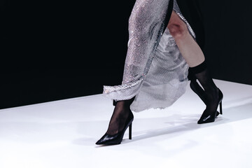 Fashion details of a long silver skirt and black high heels on a black white background. Fashion model walking the runway on Fashion week