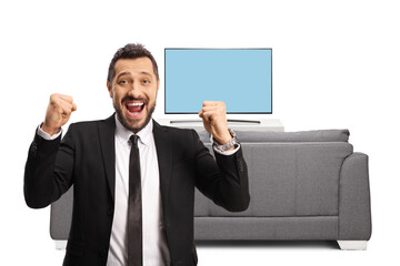 Young businessman gesturing happiness in front of tv and looking at camera