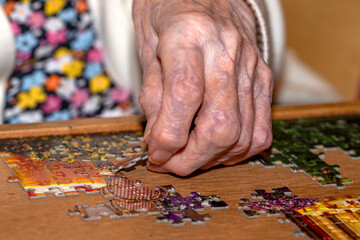 Close-up of an elderly person's hand carefully placing a jigsaw puzzle piece into a larger puzzle, focusing on the detail and care taken with the task. The person's hand shows signs of aging.