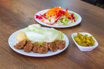 Turkish style raw meatballs, salad and pickled peppers on a wooden table.