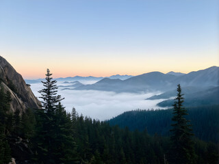 The thick morning fog wraps around the mountains, creating a serene and captivating scene of misty peaks and valleys