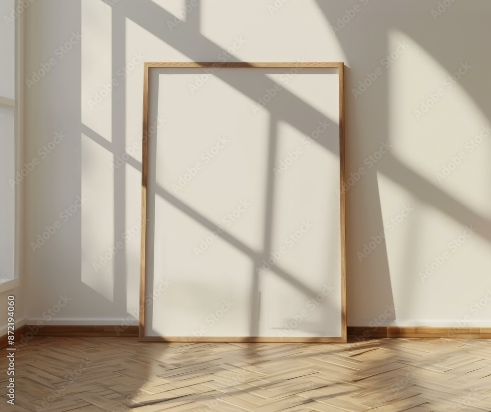 Poster an empty wooden picture frame stands on the floor in front of a white wall with shadows from the win