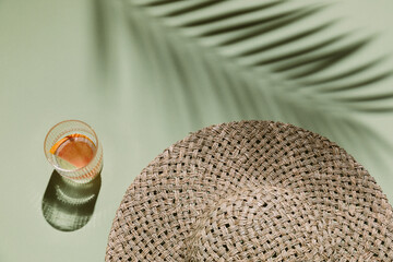 Summer flat lay with straw hat and glass of water with grapefruit slices on green background with...