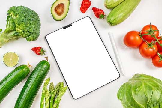 Digital tablet computer with mockup white screen on organic green vegetables vegetarian healthy foodo background.