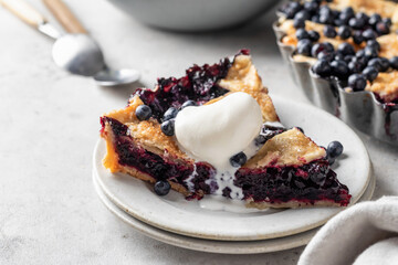 A piece of homemade blueberry pie served with a scoop of ice cream on light gray table background