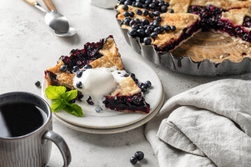 A piece of homemade blueberry pie served with a scoop of ice cream and mint on light gray table background